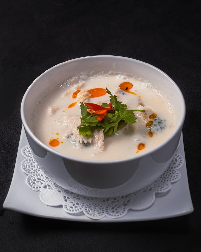 Creamy coconut soup with chicken, cilantro, and chili oil in a white bowl on a dark background.