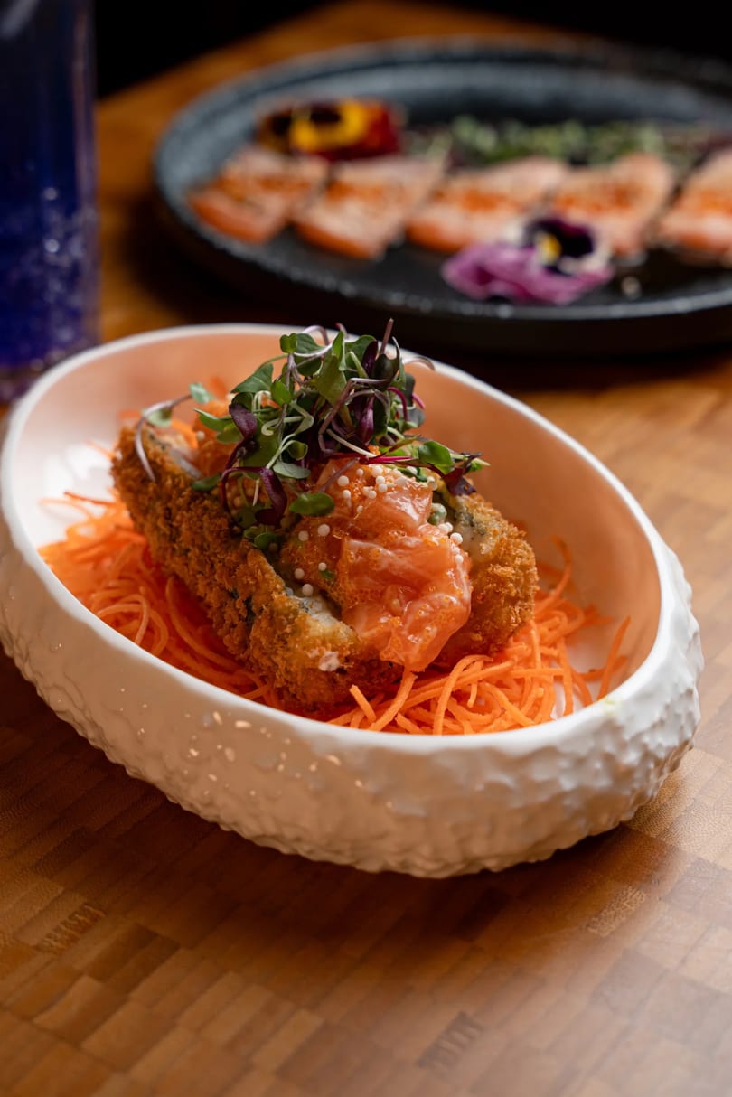 Crispy fried sushi roll topped with salmon, microgreens, and tobiko, served on shredded carrots.