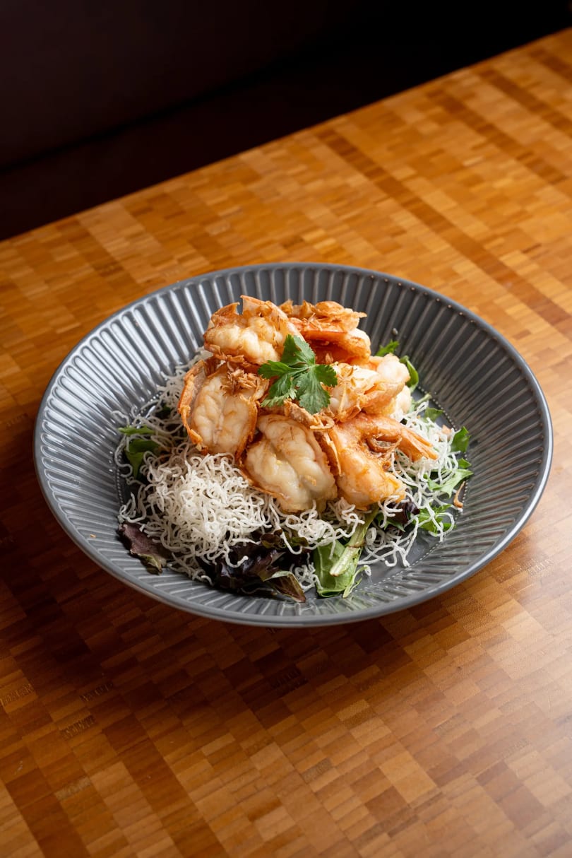 Crispy fried shrimp with vermicelli noodles and mixed greens on a gray plate.