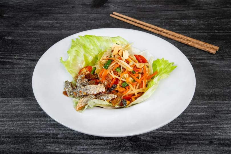 Som Tum salad with crispy fish skin and lettuce wraps on a white plate with chopsticks.