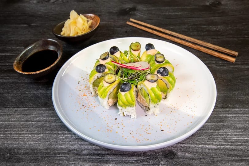 Sushi rolls with avocado, blueberries, and microgreens, served with soy sauce and pickled ginger.