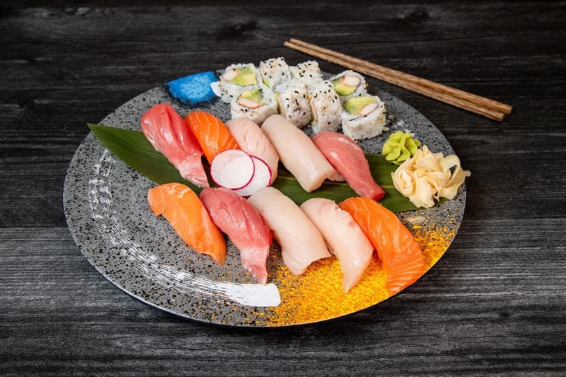 Assorted sushi and sashimi platter with California rolls, ginger, and wasabi on a dark table.