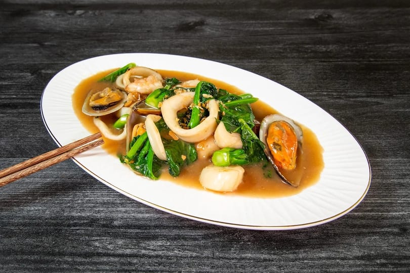 Seafood stir-fry with squid, mussels, clams, shrimp, and green vegetables in a savory sauce.